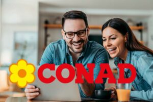 Una coppia sorridente di fronte a laptop e, in evidenza, il logo di Conad