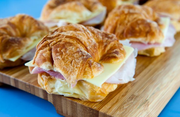 cornetti di pasta sfoglia con prosciutto e formaggio su tagliere di legno 